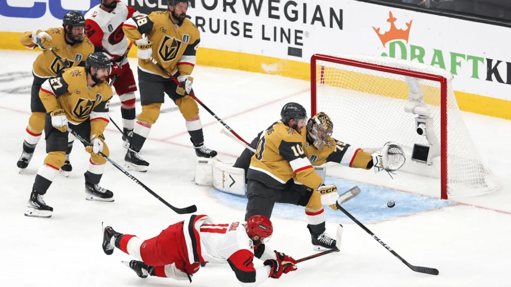 Mesmo caindo Jordan Staal (número 11), consegue tocar o puck e fazer o gol, no jogo 4 da final da Stanley Cup 2026 entre as equipes de Vegas e Carolina - CAR@VGK, SCF – Fonte: NHL (2026).