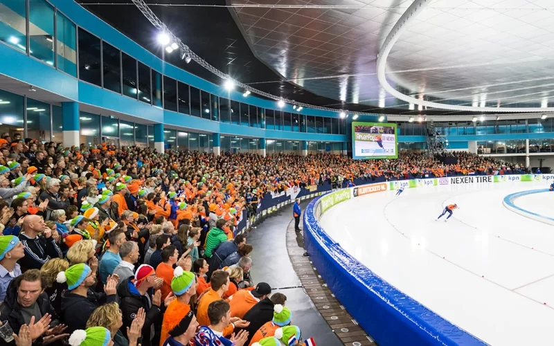 Competição de patinação de velocidade em pista longa, com a grande torcida da Holanda assistindo - Fonte: Olympics (2026)