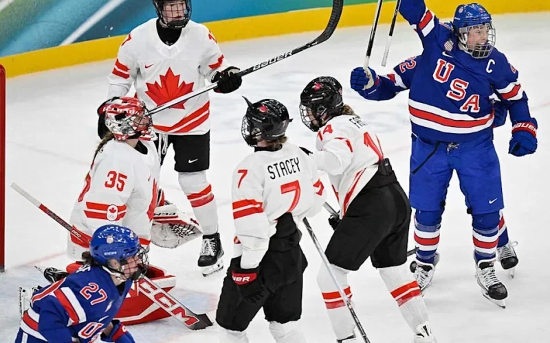 Hilary Knight da equipe dos EUA, comemora o primeiro gol de sua equipe contra Ann-Renee do Canadá durante a disputa pela medalha de ouro do hockey no gelo feminino, entre EUA e Canadá na Milano Santagiulia Ice Hockey Arena, durante os Jogos Olímpicos de Inverno Milano Cortina 2026, em 19/02/2026. FOTO: ALEXANDER NEMENOV/AFP via Getty Images – Fonte: CA Sports (2026).