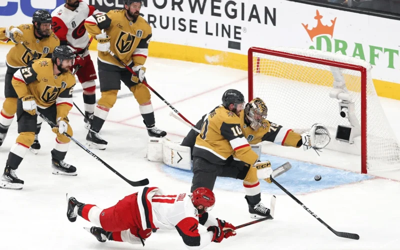 Mesmo caindo Jordan Staal (número 11), consegue tocar o puck e fazer o gol, no jogo 4 da final da Stanley Cup 2026 entre as equipes de Vegas e Carolina - CAR@VGK, SCF – Fonte: NHL (2026).